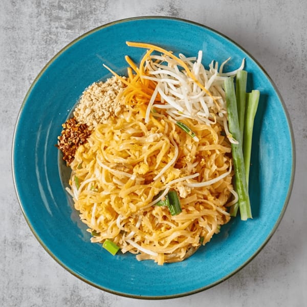 Pad Thai noodles with bean sprouts, shredded carrots, crushed peanuts, and chili flakes on a blue plate.