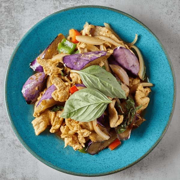 Stir-fried chicken with purple eggplant, onions, bell peppers, and basil on a blue plate.