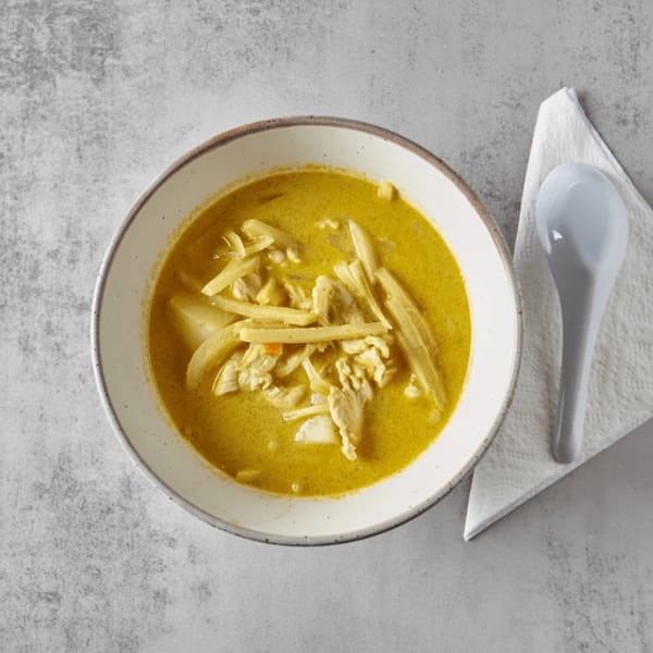 Top-down view of a bowl of yellow curry with chicken and bamboo shoots, with a spoon and napkin.