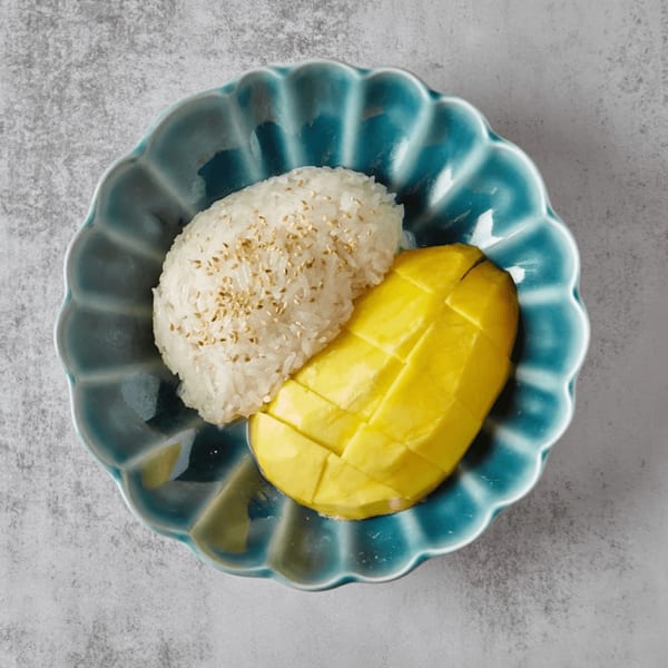 Mango sticky rice with sesame seeds on a scalloped blue plate.