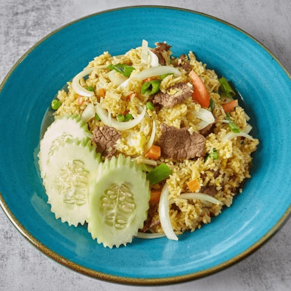 Beef fried rice with vegetables and cucumber slices on a blue plate.